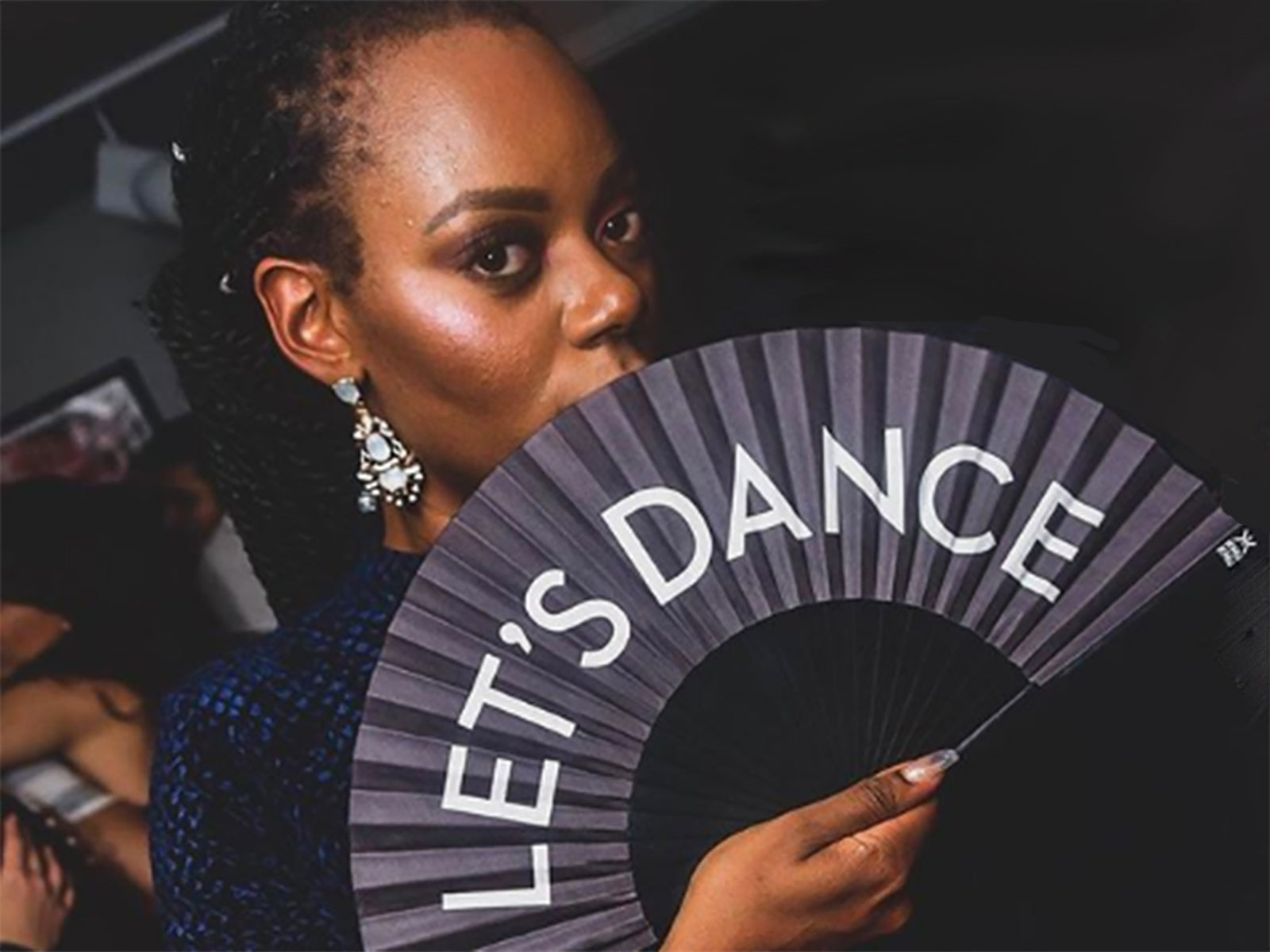 Girl wearing Khu Khu Statement Let's Dance Hand-Fan at an event. White letters on Black cotton fabric with black wooden sticks. White logo. Black rivets and fabric rim. 